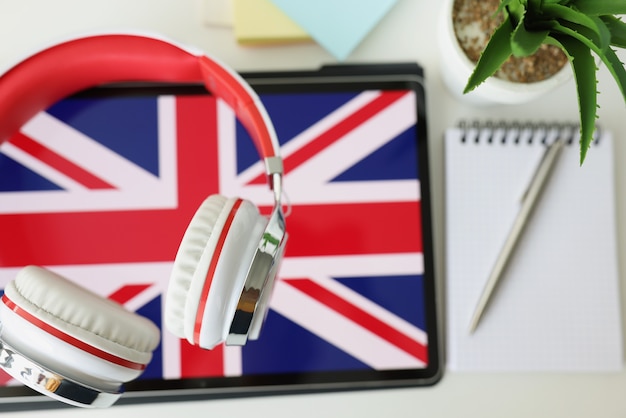 Tablet met afbeelding van britse vlag met koptelefoon en notebook met pen liggen op tafel on