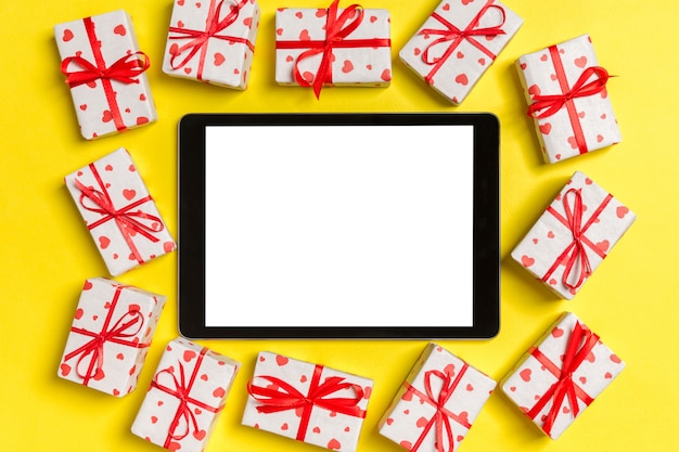 tablet omgeven door geschenkdozen met harten inpakpapier op geel