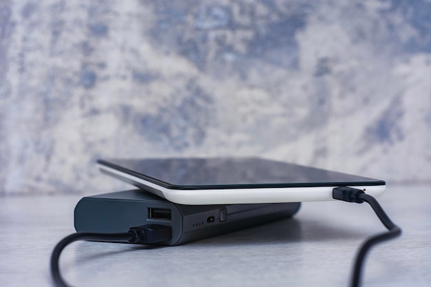 Foto tablet opladen met powerbank op een grijze houten tafel draagbare oplader voor het opladen van apparaten