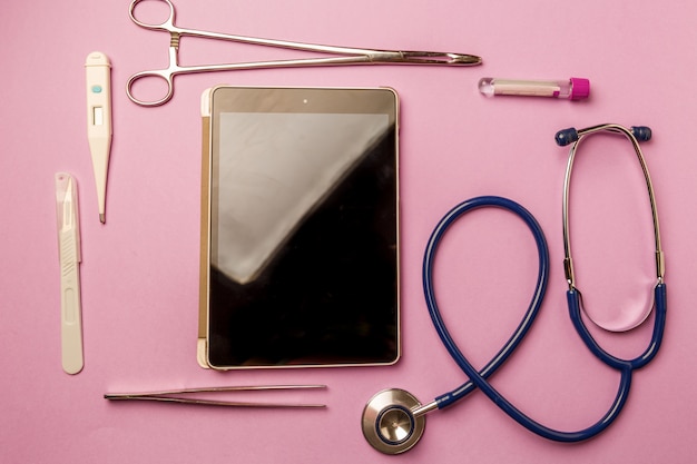 Tablet pc and doctor tools on pink surface