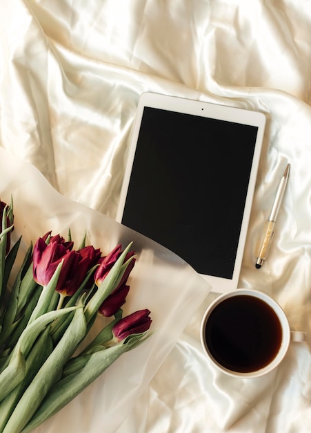 Tablet, pioenrozen en koffie op bed