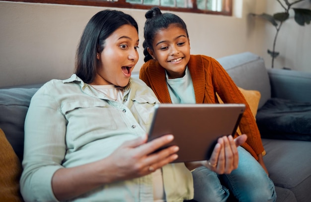 Tablet pregnant mother and girl on technology looking at children education development app Learning video relax and happy family together on a home living room sofa watching a cartoon with mama