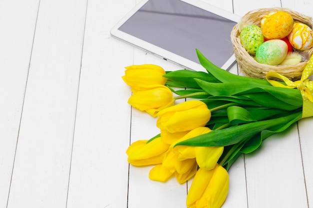 Tablet screen  message and colorful tulips and easter eggs on wooden