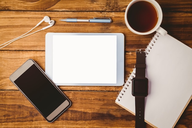 Tablet and smartphone and swatch on notepad next to cup of coffee 