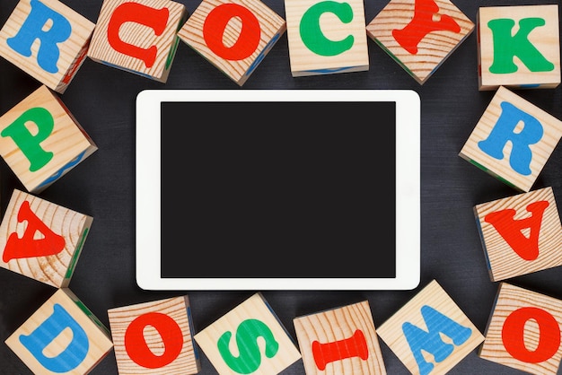 Tablet touchpad with colorful alphabet wooden blocks on black background flat lay