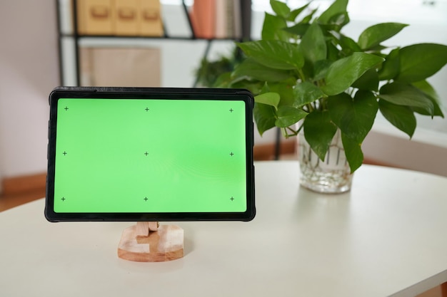 Фото Планшет с пустым зеленым экраном на деревянном держателе, стоящем на белом столе