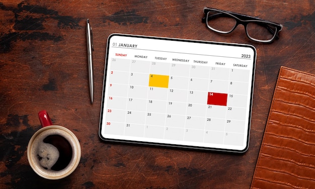 カレンダー アプリのコーヒー カップと事務用品を備えたタブレット