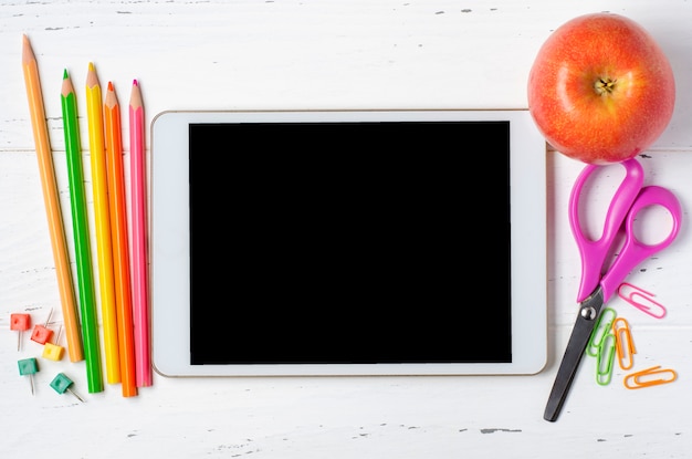 tablet with an empty screen and office supplies on a white wooden background. Concept app for school children or online learning for children. Copy space