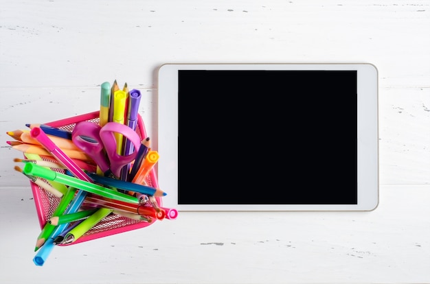 흰색 나무 바탕에 빈 화면 및 사무 용품 태블릿. 학교 어린이 또는 온라인 학습을위한 개념 앱. 공간을 복사하십시오.