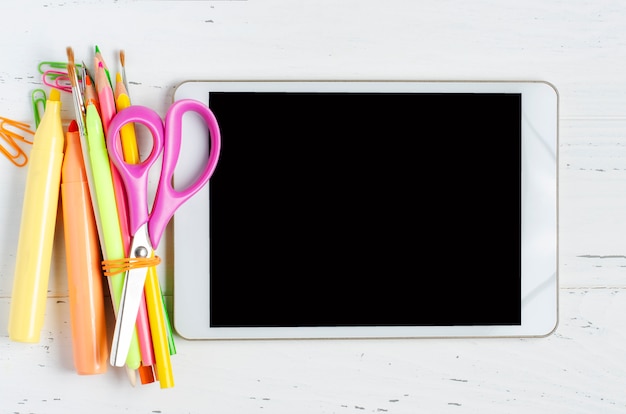 A tablet with an empty screen and office supplies on a white wooden.