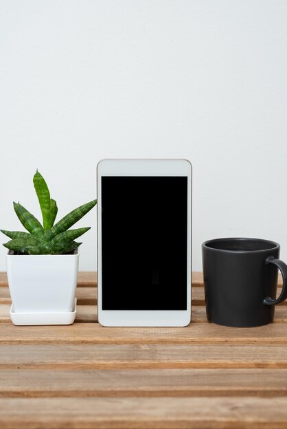 花とマグカップと机の上の携帯電話の画面に提示された植物とコーヒーの重要な発表とテーブルの上の重要な情報を持つタブレット