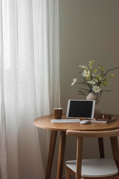 A tablet with a keyboard a glass a vase with a floral arrangement on a round table in the living room