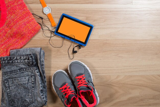 A tablet with some clothes and acessories flatlay on wooden background