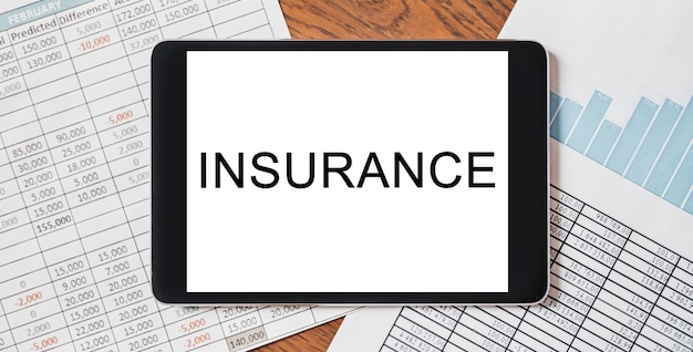 Tablet with text INSURANCE on your desktop with documents, reports and graphs. Business and finance concept