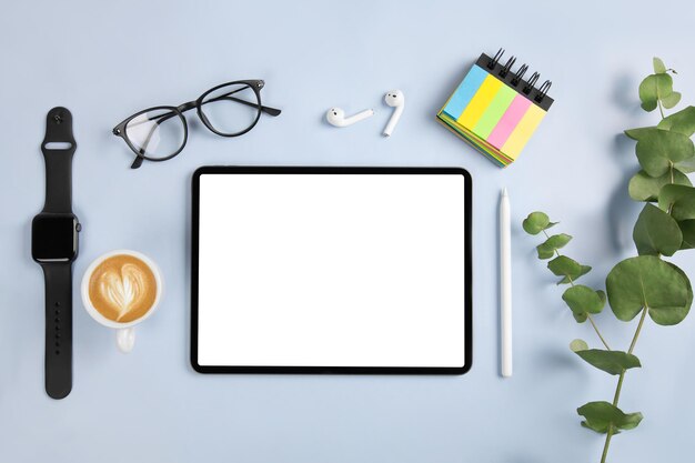 Photo tablet with white screen, pencil and watch on blue color background. flatlay. office background