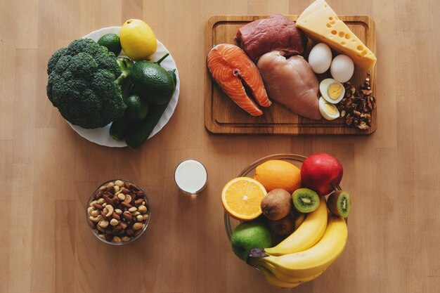 Tabletop photo of meat products vegetables fruit and nuts arranged on the wooden surface