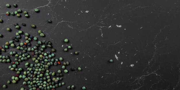 Tabletop view, Black pepper (Piper nigrum) spice spilled on dark marble like board. Turkish green / blue peppercorn variant. Banner with space for text on right.