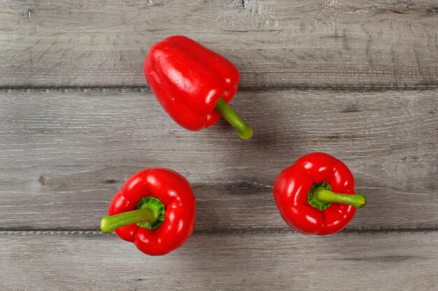 Tabletop view - three red bell peppers on gray wood desk.