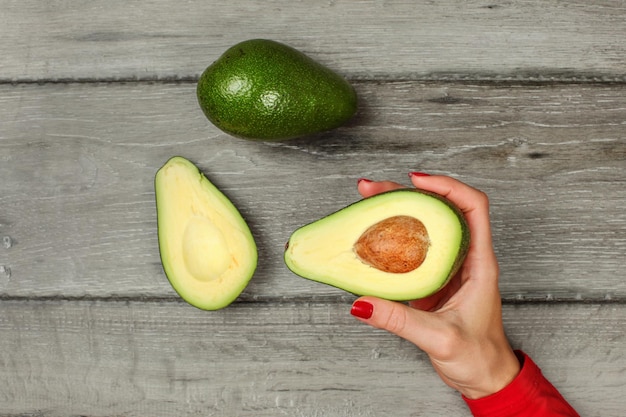 Tabletop view, woman hand holding avocado cut in half with whole pear above.