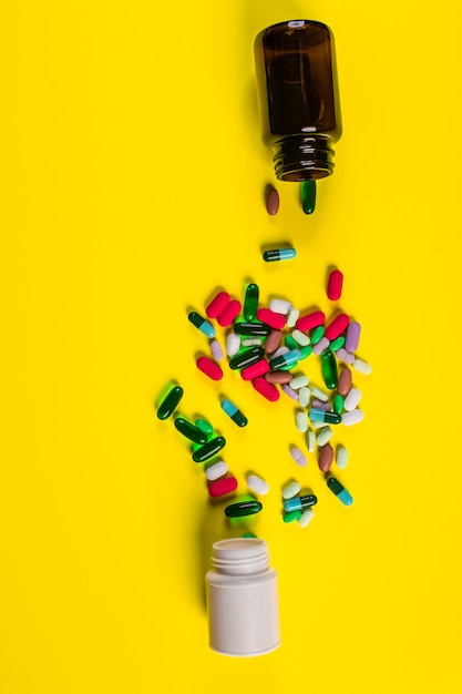 Tablets and capsules scattered from a white and brown jar on a yellow .Health . 