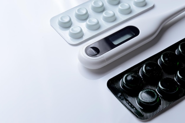 Tablets in a package and a white electronic thermometer on a white surface close-up.