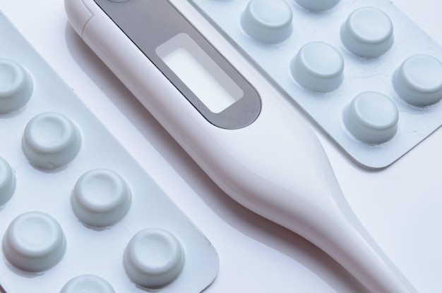 tablets in a package and a white electronic thermometer on a white surface close-up.