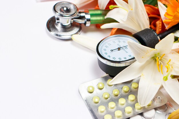 Tablets, sphingomanometer and phonendoscope with flowers on white.