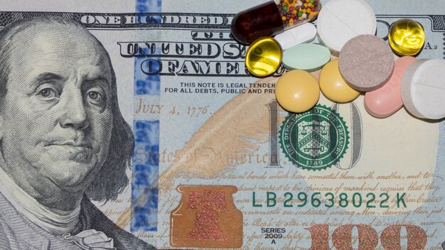 Foto tabletten en capsules van verschillende kleuren op het honderd-dollarbiljet, bovenaanzicht