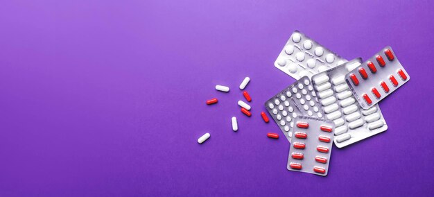 Tabletten pillen en rood-witte capsules verpakt en verspreid Bovenaanzicht lila achtergrondbanner met kopieerruimte