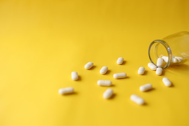 Tabletten voor vitamine of medicatie gegoten uit een glas op gele achtergrond Creatief plat leggen