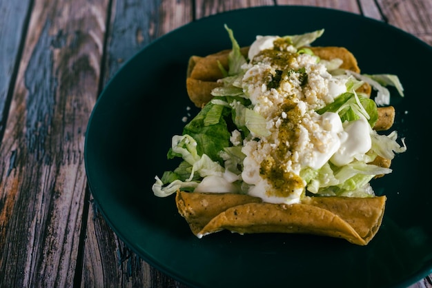 Tacos flauta with cheese cream and lettuce on a wooden table Mexican snacks