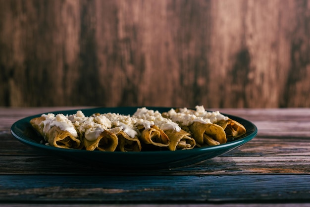 Tacos flauta with cheese and cream on a wooden table Mexican snacks