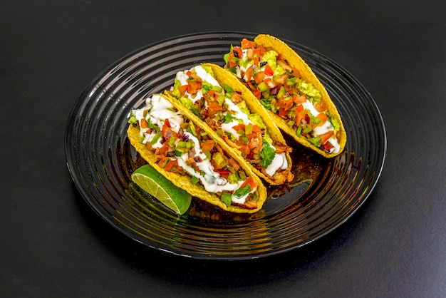 Tacos mexicanos con todo dentro de una tortilla de maiz crocante con lima sobre un plato negro