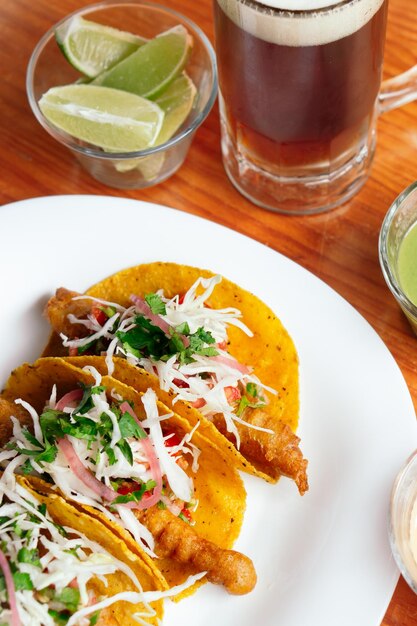 Tacos on a table with beer, lemon and salsa.