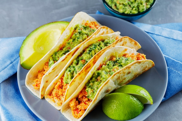Tacos with fried minced meat and guacamole on a gray plate.\
mexican tacos and lime slices on a gray background. mexican food.\
copy space