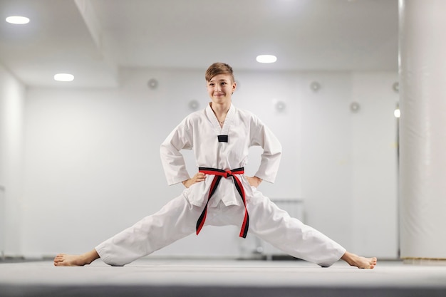 Taekwondo boy with spread legs wearing kimono and posing at martial art school