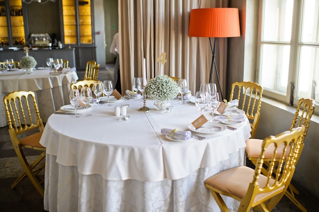 Tafel bij het bruiloftsbanket in het restaurant, klassieke stijl met witte tafelkleden en servetten, vazen met bloemen.