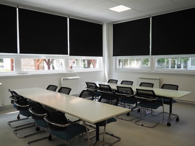 Tafel en stoelen in de vergaderruimte op kantoor in de klas of in de bibliotheekzaal Witte zwarte en grijze verf in het interieur Zwarte jaloezieën om de kamer te verduisteren Modern interieurontwerp