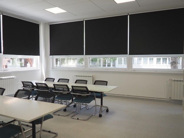 Tafel en stoelen in de vergaderruimte op kantoor in de klas of in de bibliotheekzaal Witte zwarte en grijze verf in het interieur Zwarte jaloezieën om de kamer te verduisteren Modern interieurontwerp