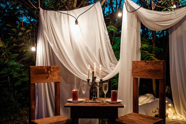 Tafel in het bos, romantisch diner voor twee bij kaarslicht. Witte gordijnen aan de boom