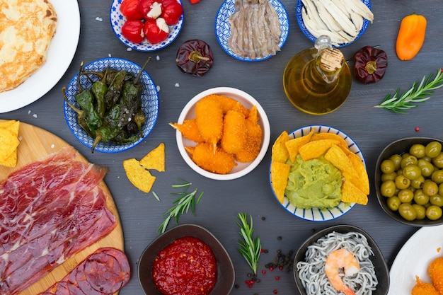 Tafel met Spaanse tapas - ansjovis, groene paprika padron, jamon, kroketten, guacamole en olijven