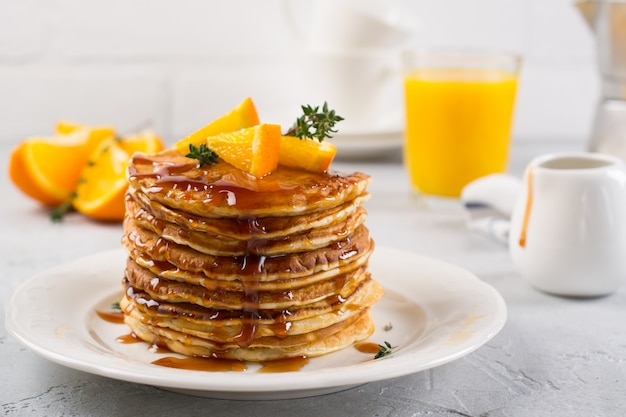 Tafel van ontbijt. Pannenkoeken met sinaasappel en besprenkelde ahornsiroop, sinaasappelsap en koffie