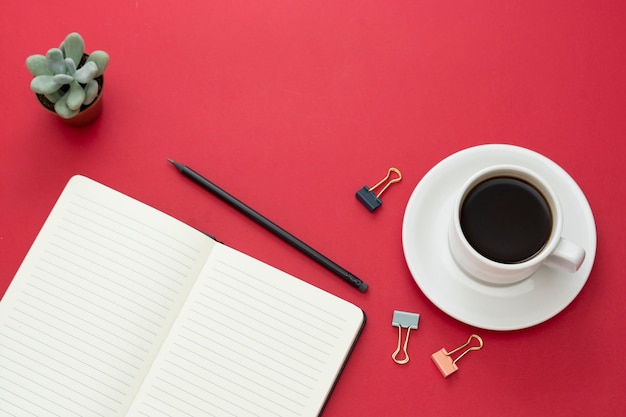 Tafelblad, bureau met open laptop en koffiekopje op rode achtergrond. Ruimte voor tekst kopiëren.