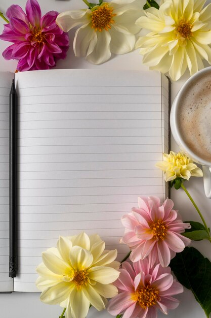 Foto tafelblad van een werkruimte met prachtige dahlia-bloemen, koffiekopje en een notitieboekje, kopieerruimte.