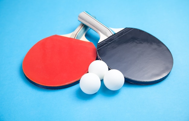 Tafeltennisrackets en witte plastic ballen op een blauwe achtergrond.