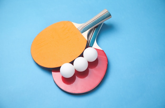 Tafeltennisrackets en witte plastic ballen op een blauwe achtergrond.