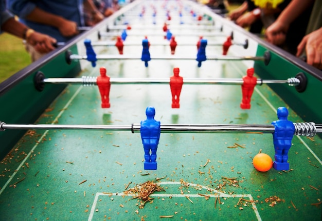 Tafelvoetbal spelen en mensen buiten met tafelspel of close-up op competitie met pingpongbal voetbalbord en kleine plastic voetbalspelers of speelgoed voor sociaal evenement of sport in pub voor de lol