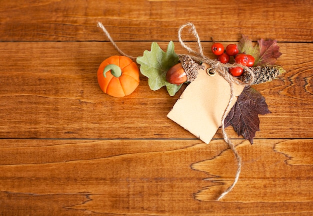 tag with leaves, berries and pumpkin on a wooden table. View from above