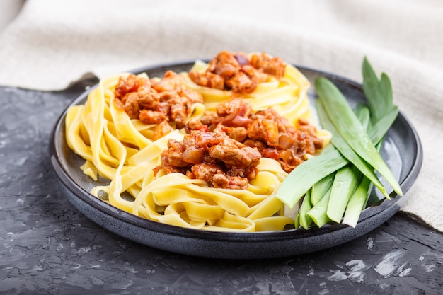 Tagliatelle bolognese pasta with minced meat on a black concrete.