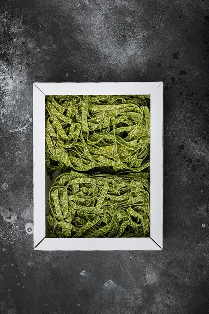 Tagliatelle green pasta pack set, on black dark stone table\
background, top view flat lay